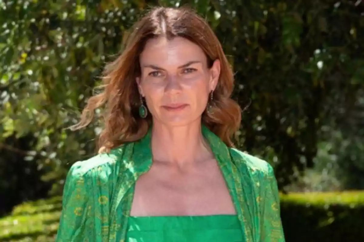 Mujer con cabello castaño y ondulado, vestida con un conjunto verde, posando al aire libre con árboles de fondo.