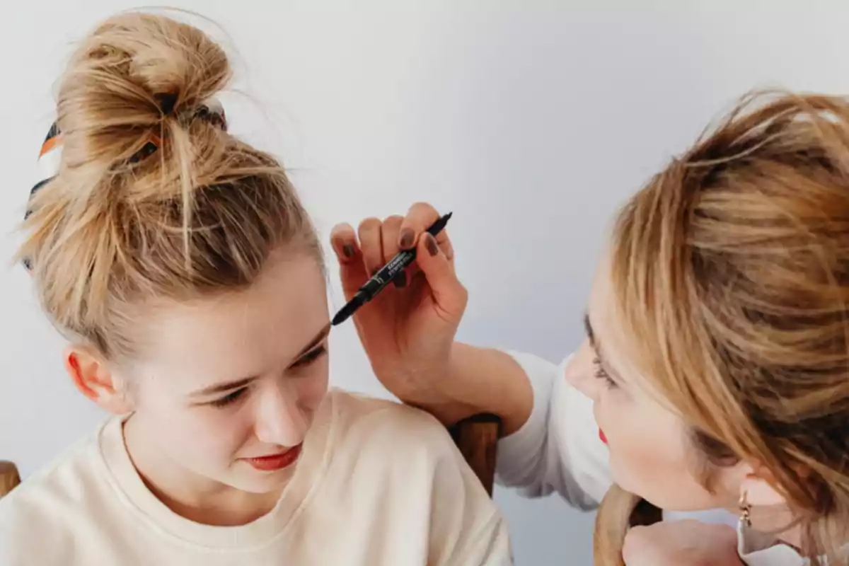 Una persona está aplicando maquillaje en las cejas de otra persona con un lápiz de cejas.