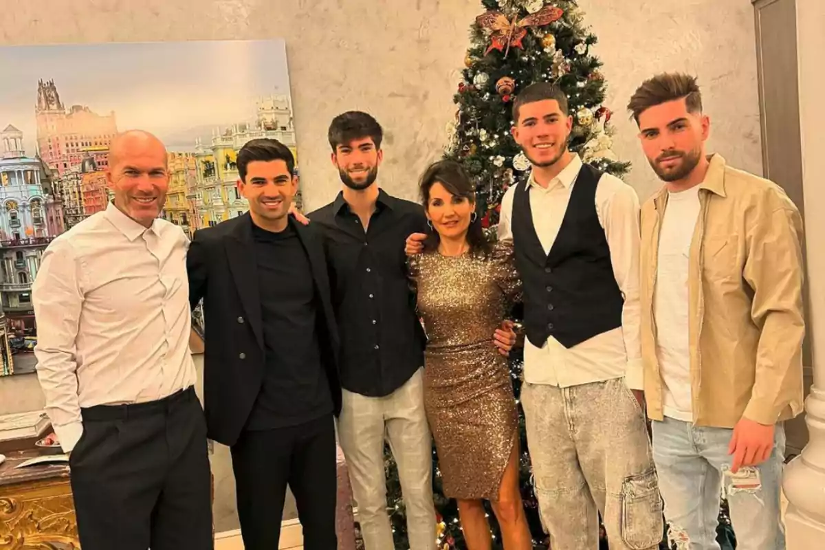 Una familia posando juntos frente a un árbol de Navidad decorado, con una pintura de una ciudad en el fondo.