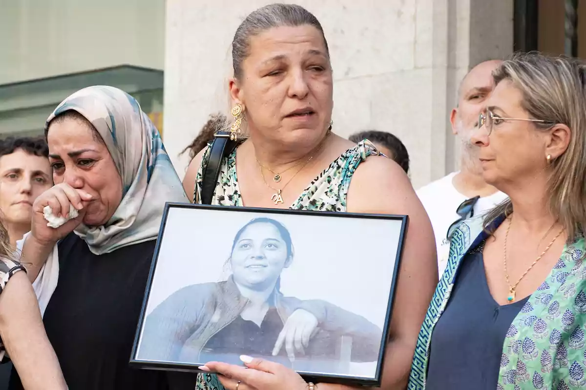 Un grupo de personas, algunas visiblemente emocionadas, sostienen una fotografía en blanco y negro de una mujer joven.