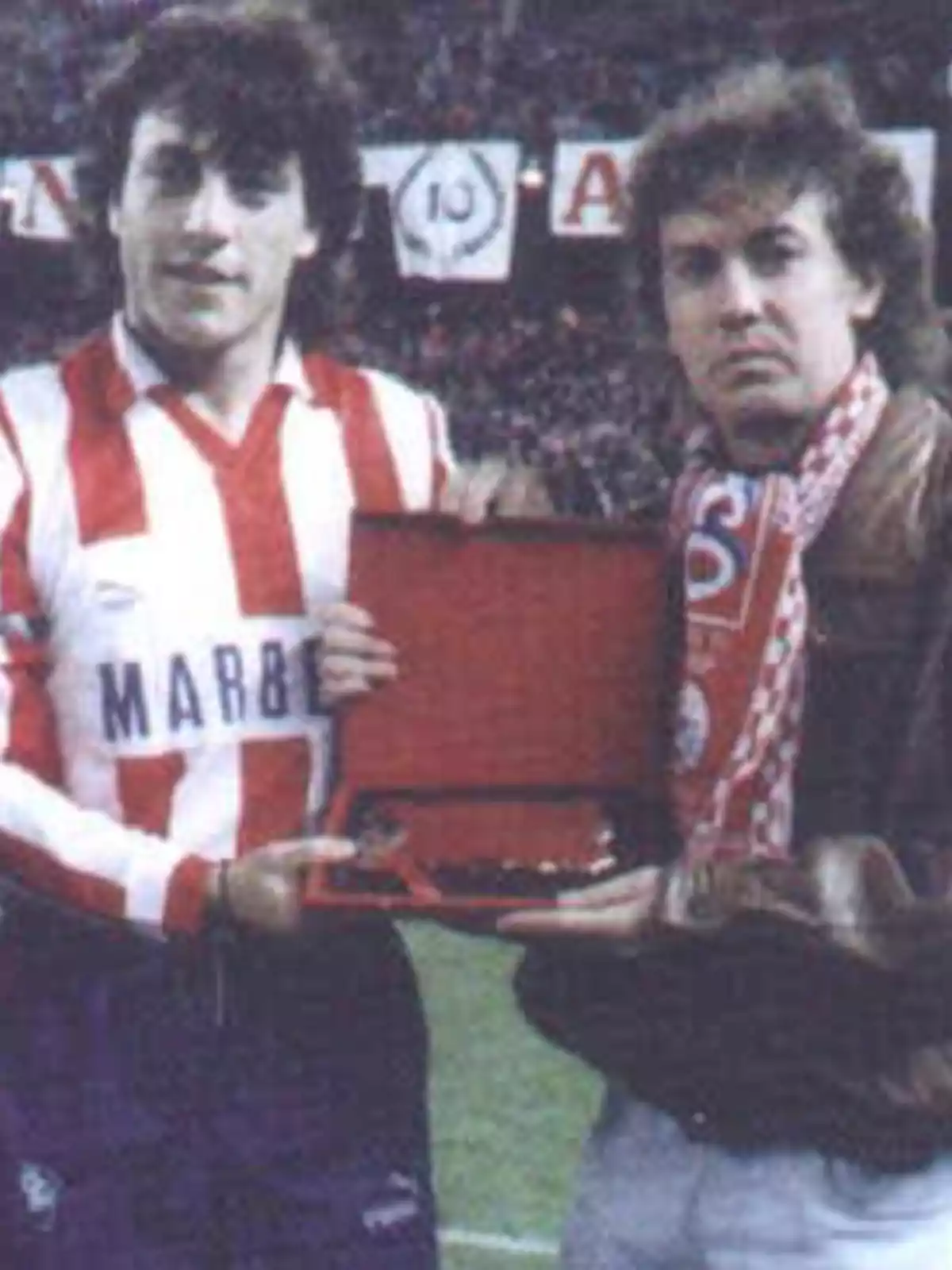 Dos personas sosteniendo un estuche rojo en un estadio de fútbol.