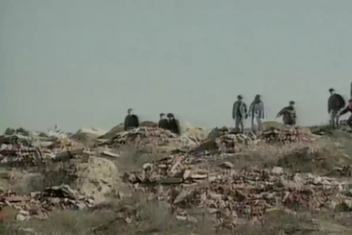 Un grupo de personas camina sobre un terreno lleno de escombros y basura bajo un cielo despejado.