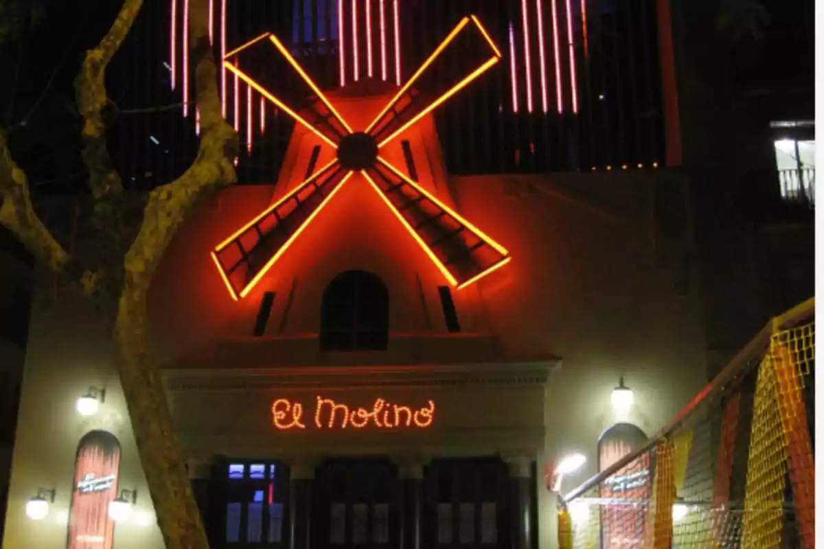 Fachada iluminada de un edificio con un molino de viento en neón rojo y el letrero "El Molino" en la entrada.