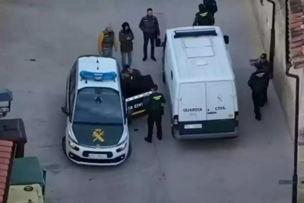 Un grupo de personas, algunas con uniformes de la Guardia Civil, están junto a dos vehículos oficiales en una calle.