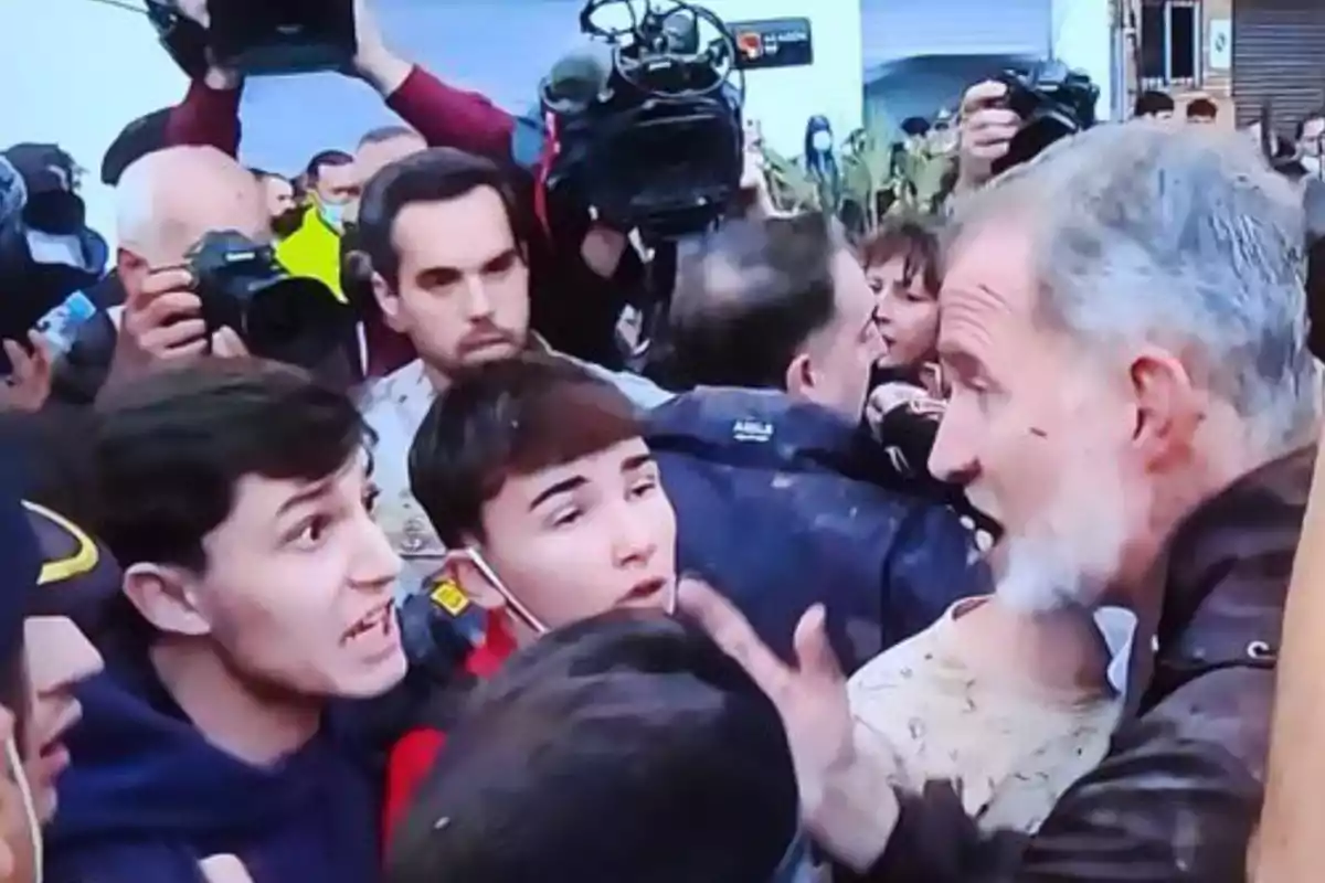 Un grupo de personas discute en medio de una multitud con cámaras y fotógrafos alrededor.