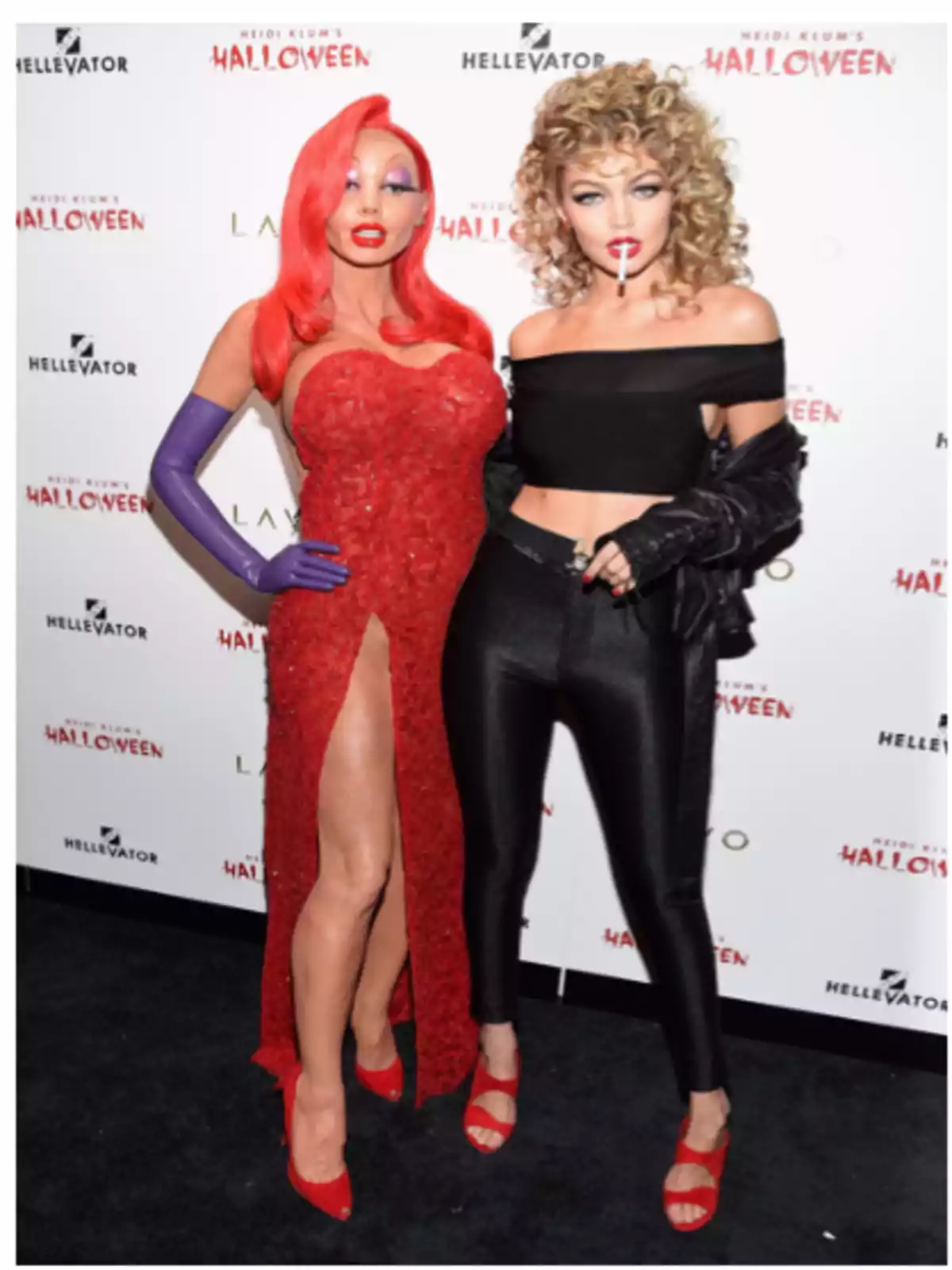 Dos personas posan en un evento de Halloween, una vestida como Jessica Rabbit con un vestido rojo brillante y guantes morados, y la otra con un atuendo negro ajustado y una chaqueta de cuero.