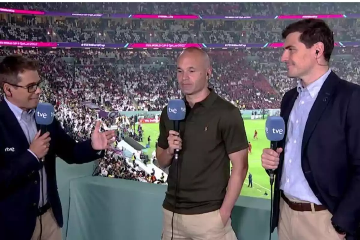 Tres personas con micrófonos de TVE están en un estadio lleno de espectadores durante un evento deportivo.