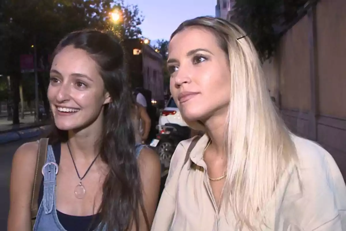 Dos mujeres sonrientes en una calle iluminada por luces nocturnas.