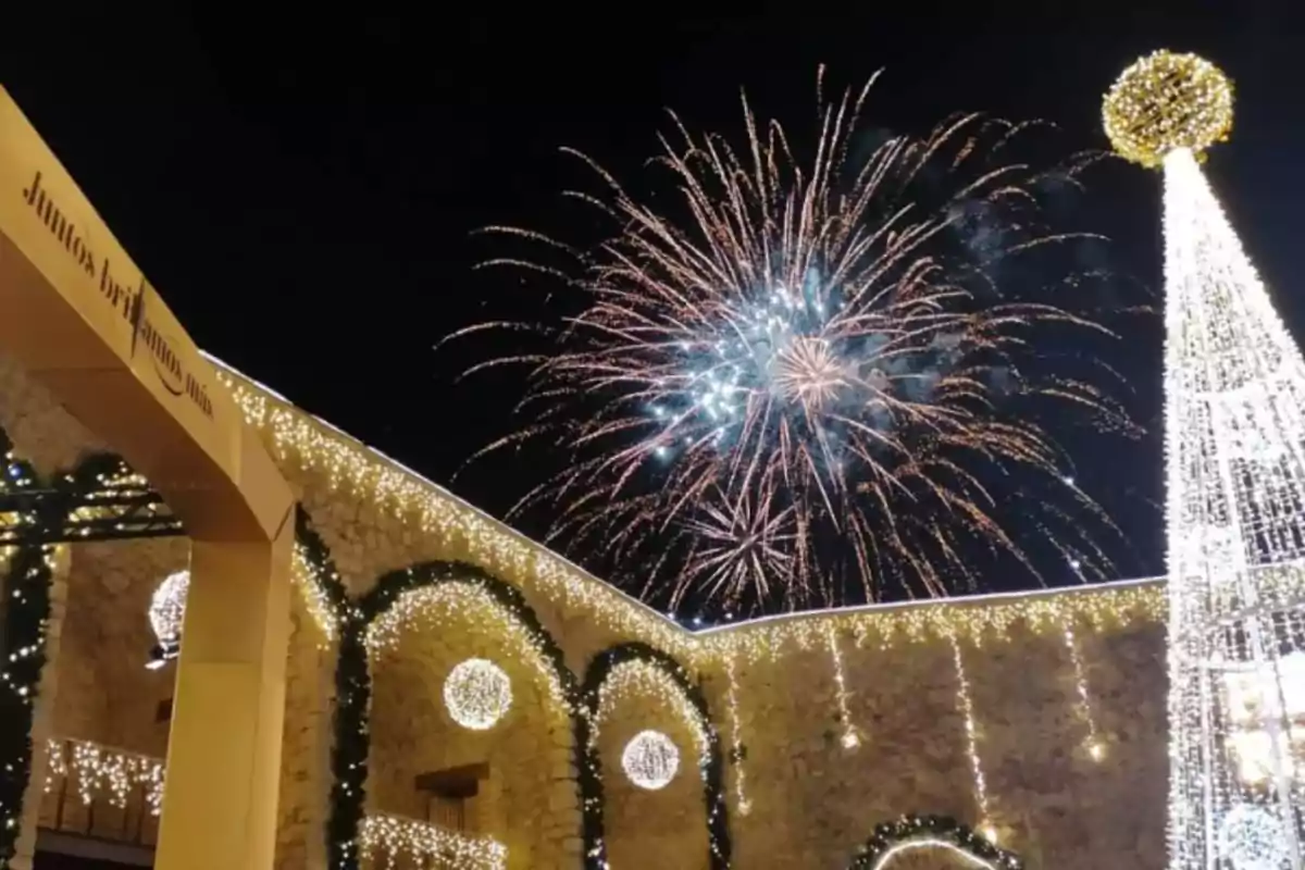 Celebración nocturna con fuegos artificiales y luces navideñas adornando un edificio de piedra.