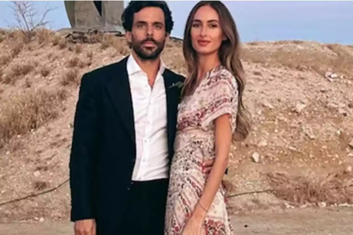 Una pareja posando al aire libre en un entorno natural con un fondo de tierra y vegetación seca.