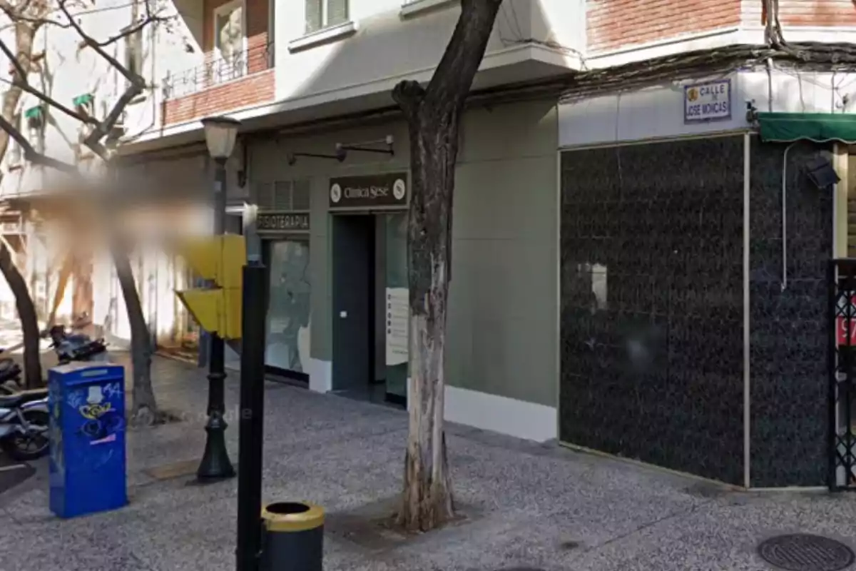 Fachada de un edificio urbano con una clínica y un árbol en la acera.