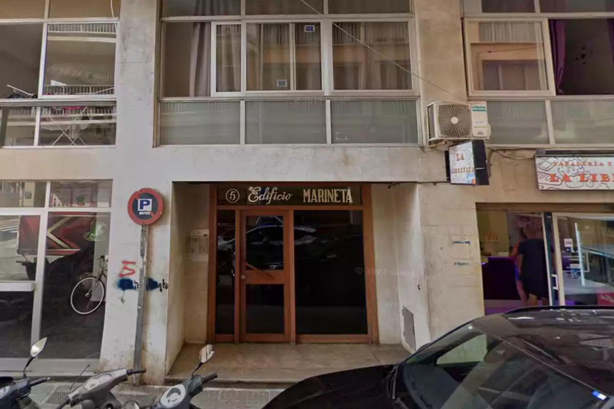 Entrada del Edificio Marinetá con un letrero y un cartel de prohibido estacionar al lado, junto a una calle con bicicletas y motocicletas estacionadas.