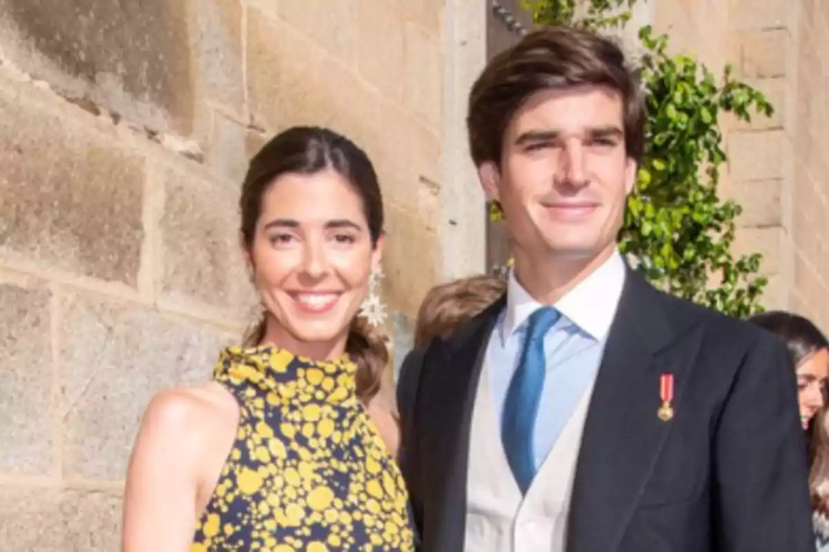 Una pareja sonriente posando frente a una pared de piedra en un evento formal.