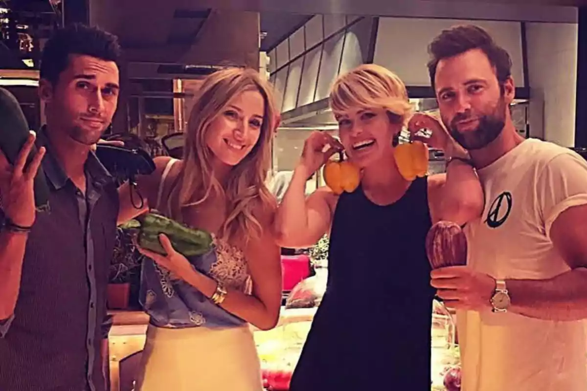 Un grupo de cuatro personas posando con diferentes vegetales en un ambiente interior.