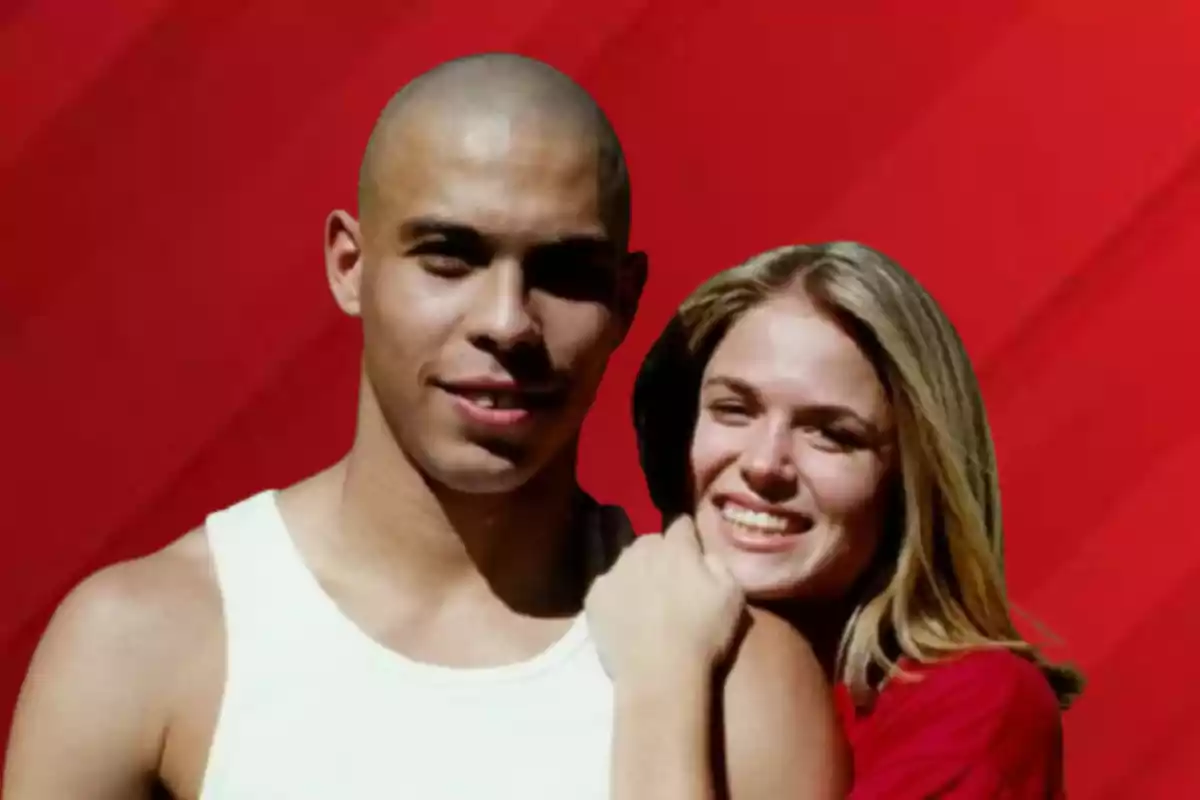 Una pareja sonriente posando frente a un fondo rojo.