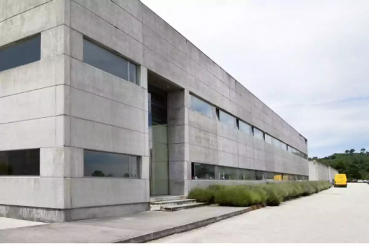 Edificio moderno de concreto con ventanas alargadas y un camino pavimentado al frente.