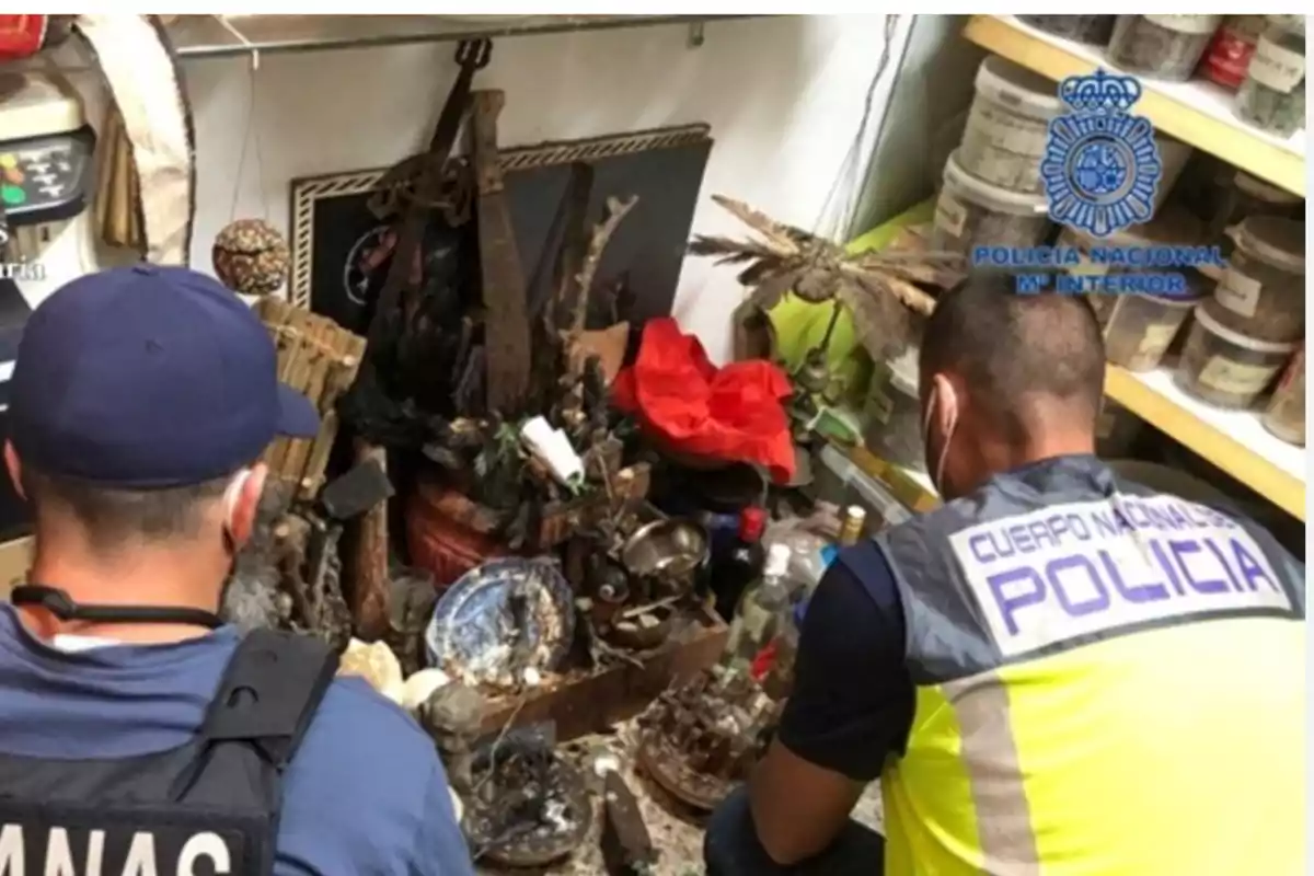 Dos agentes de policía inspeccionan un altar con diversos objetos rituales y ofrendas en un espacio cerrado.