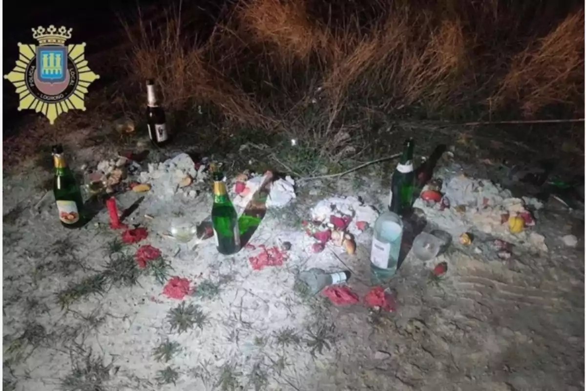 Botellas de vidrio y restos de comida esparcidos en el suelo junto a un escudo de la policía local.