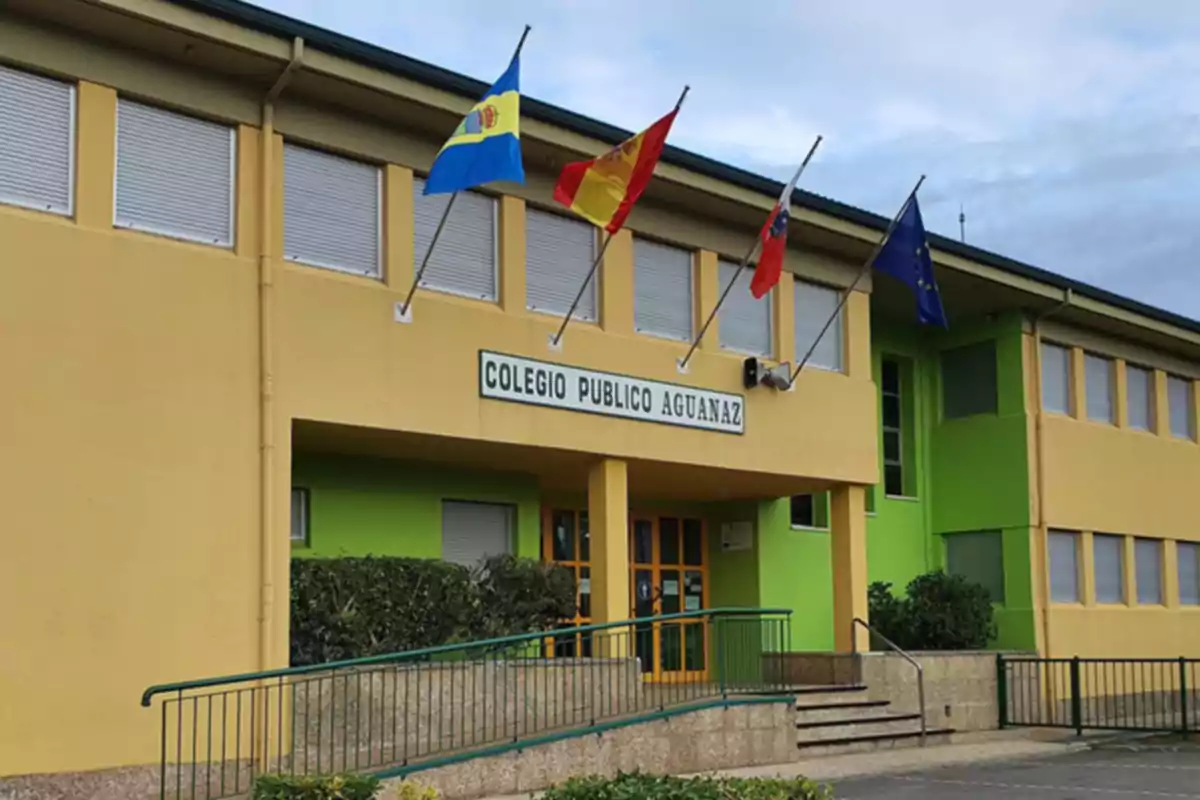 Fachada de un colegio público con varias banderas en el exterior.