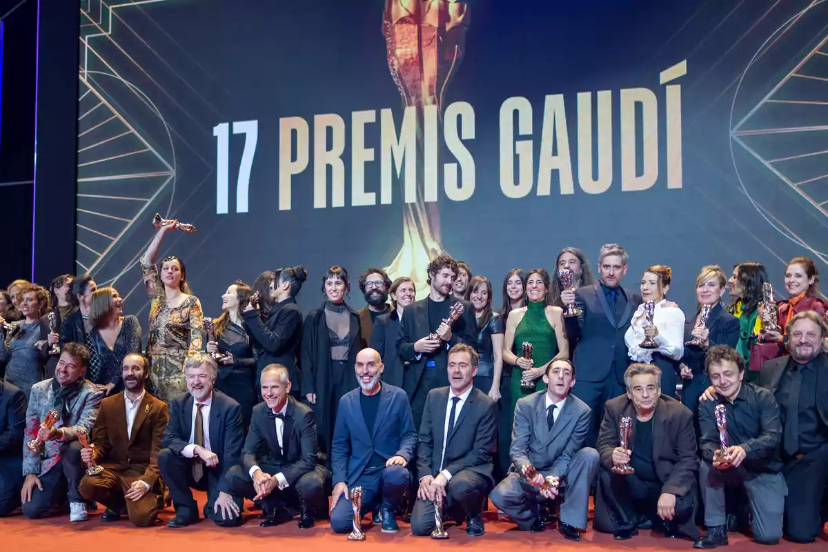 Un grupo de personas posando con trofeos en un evento de premios cinematográficos, con un gran cartel de fondo que dice "17 Premis Gaudí".