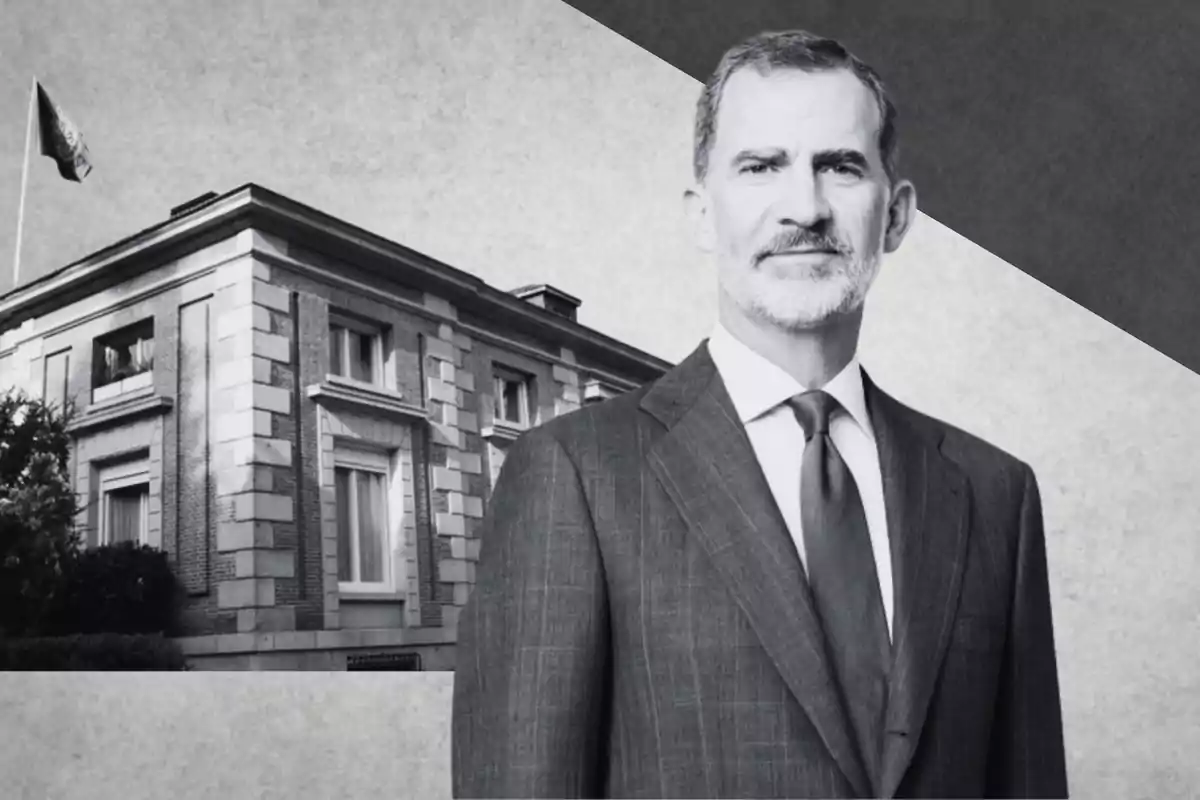 Un hombre con traje y corbata frente a un edificio de estilo clásico con una bandera ondeando en el techo.