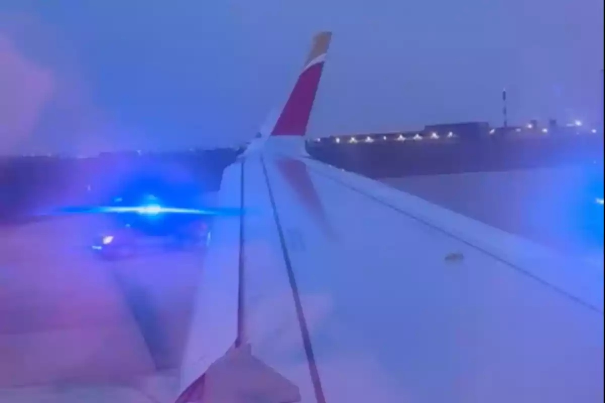 Un avión en la pista con luces azules de emergencia reflejadas en la ventana.