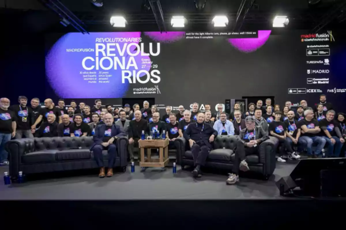 Un grupo de personas posando juntas en un evento con un gran cartel de fondo que dice "Revolucionarios" y "Madrid Fusión".