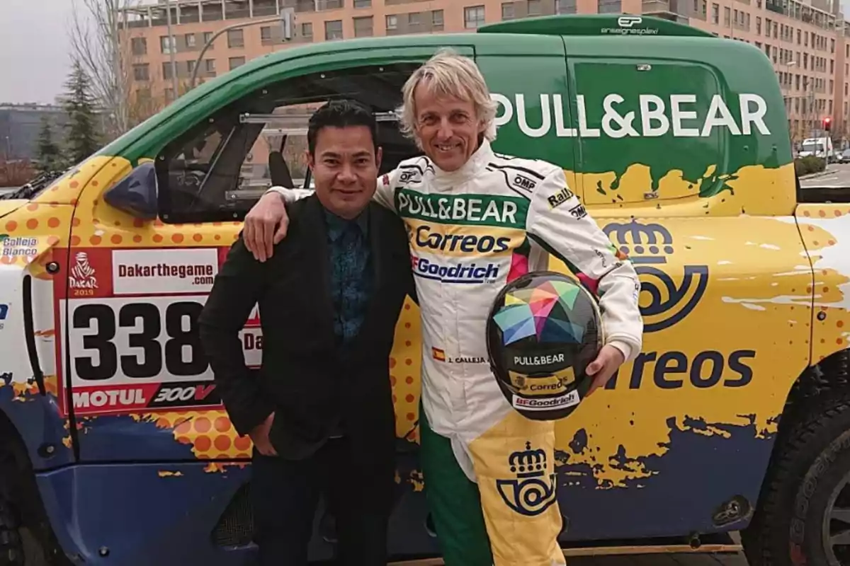 Dos personas posan junto a un vehículo de carreras decorado con logotipos de patrocinadores.