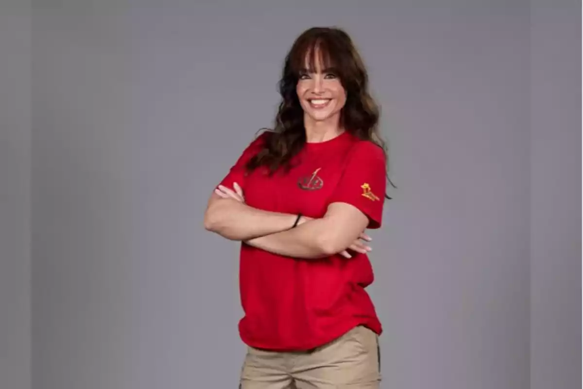 Mujer con camiseta roja y pantalones beige, sonriendo con los brazos cruzados.