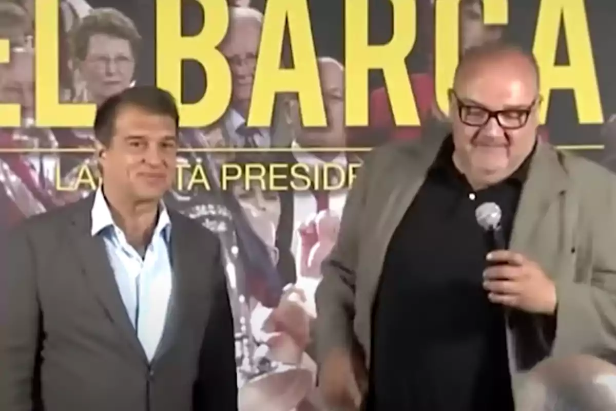 Dos hombres de pie frente a un cartel con letras amarillas, uno de ellos sostiene un micrófono. Dos hombres de pie frente a un cartel con letras amarillas, uno de ellos sostiene un micrófono.