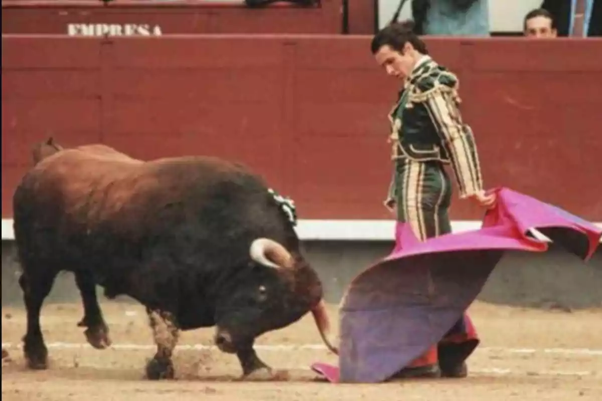 Un torero en la plaza de toros sostiene un capote mientras un toro se aproxima.