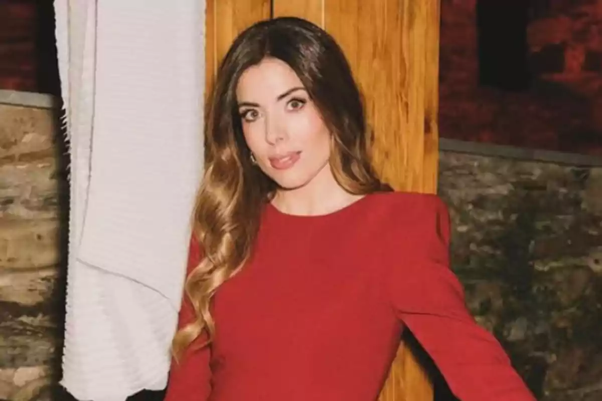 Una persona con vestido rojo posando junto a una pared de madera.