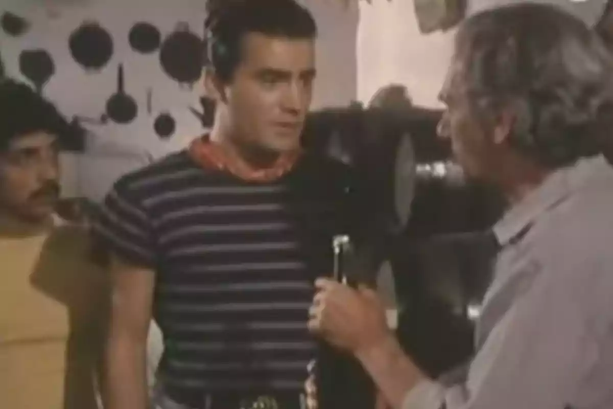 Tres hombres conversan en una habitación con utensilios de cocina colgados en la pared. Tres hombres conversan en una habitación con utensilios de cocina colgados en la pared.