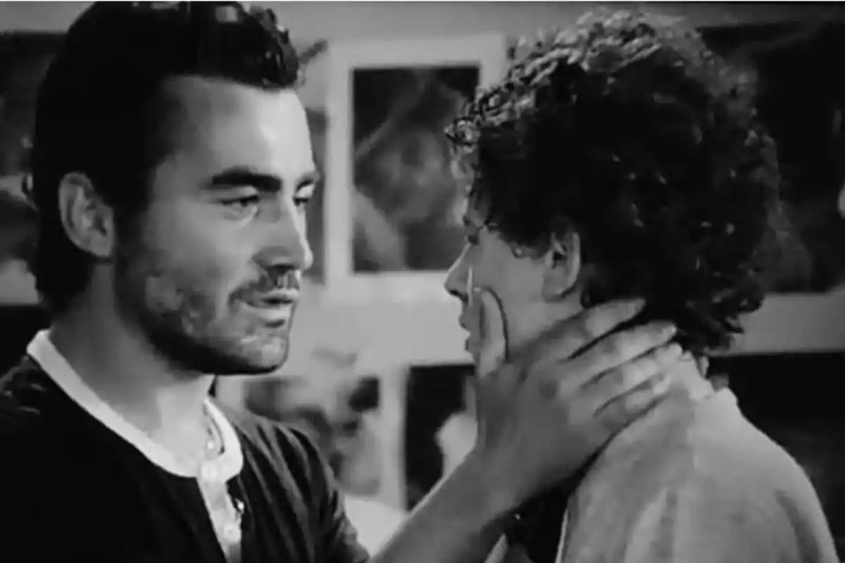 Dos personas en una escena en blanco y negro, una de ellas sostiene el rostro de la otra con una expresión seria. Dos personas en una escena en blanco y negro, una de ellas sostiene el rostro de la otra con una expresión seria.