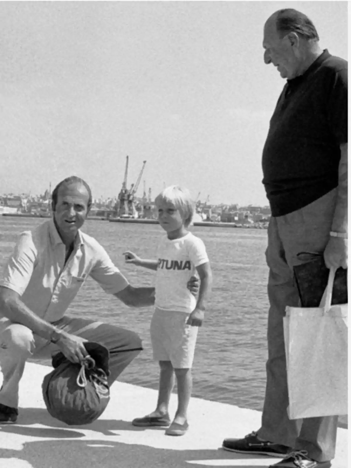Tres personas están en un muelle junto al agua, una de ellas es un niño con una camiseta que dice Tres personas están en un muelle junto al agua, una de ellas es un niño con una camiseta que dice