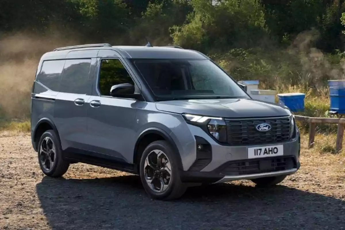 Una furgoneta Ford gris estacionada en un camino de tierra con árboles y colmenas al fondo. Una furgoneta Ford gris estacionada en un camino de tierra con árboles y colmenas al fondo.