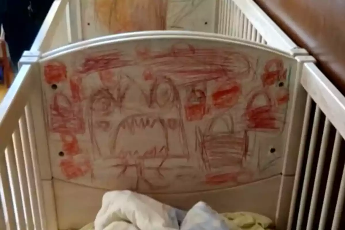 Una cuna blanca con dibujos infantiles en el respaldo hechos con crayones de colores rojo y marrón. Una cuna blanca con dibujos infantiles en el respaldo hechos con crayones de colores rojo y marrón.