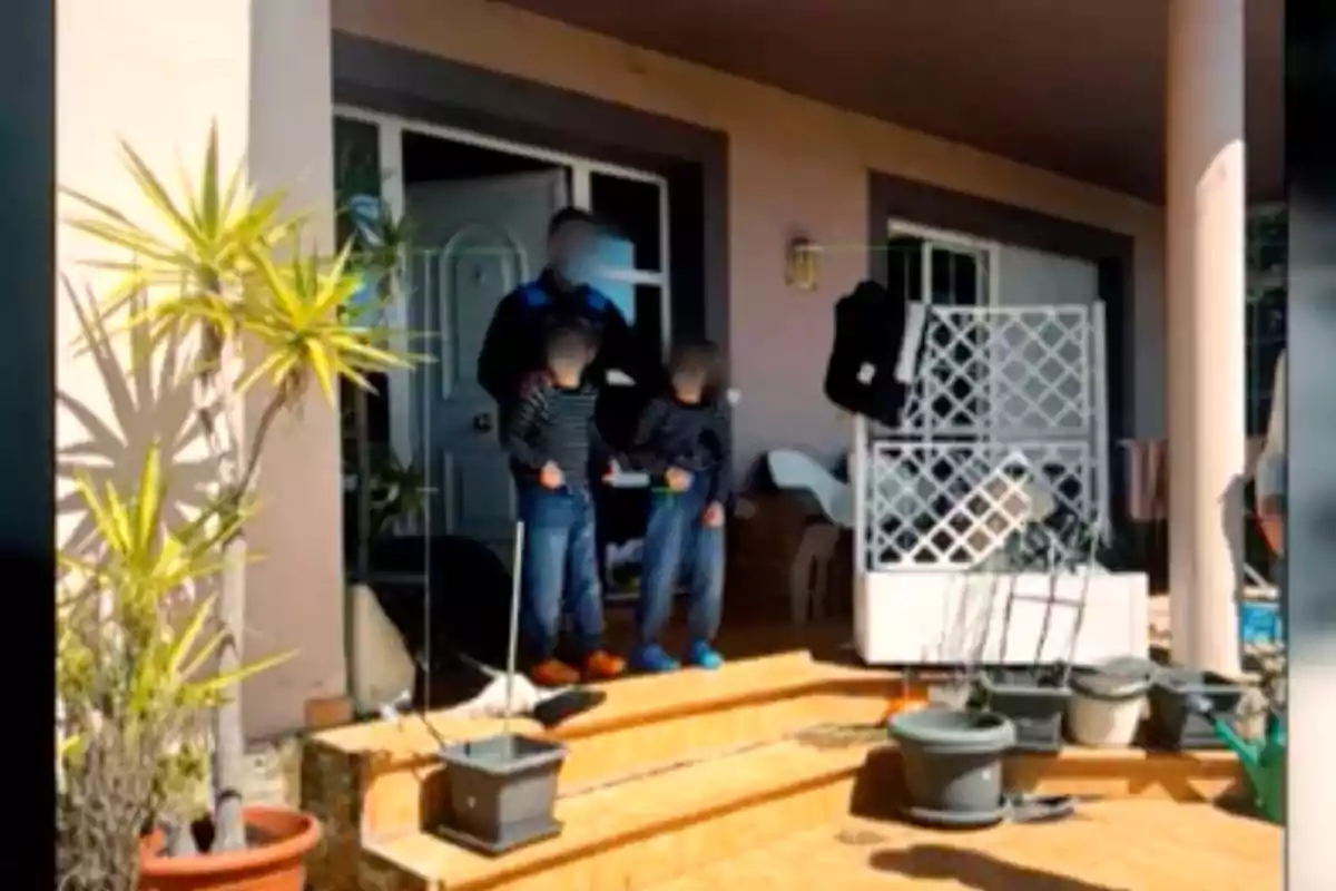 Una persona y dos niños están de pie en la entrada de una casa, rodeados de macetas y plantas. Una persona y dos niños están de pie en la entrada de una casa, rodeados de macetas y plantas.