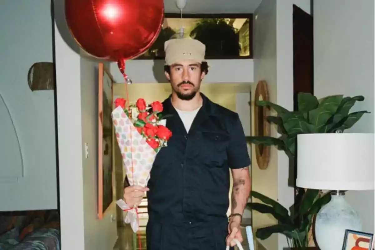 Hombre con gorra y barba sosteniendo un ramo de flores y un globo rojo en una habitación con plantas y lámpara.
