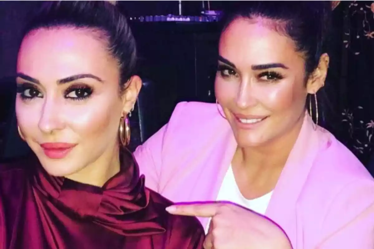Dos mujeres posando juntas, una de ellas señalando a la otra, ambas con maquillaje y pendientes grandes. Dos mujeres posando juntas, una de ellas señalando a la otra, ambas con maquillaje y pendientes grandes.