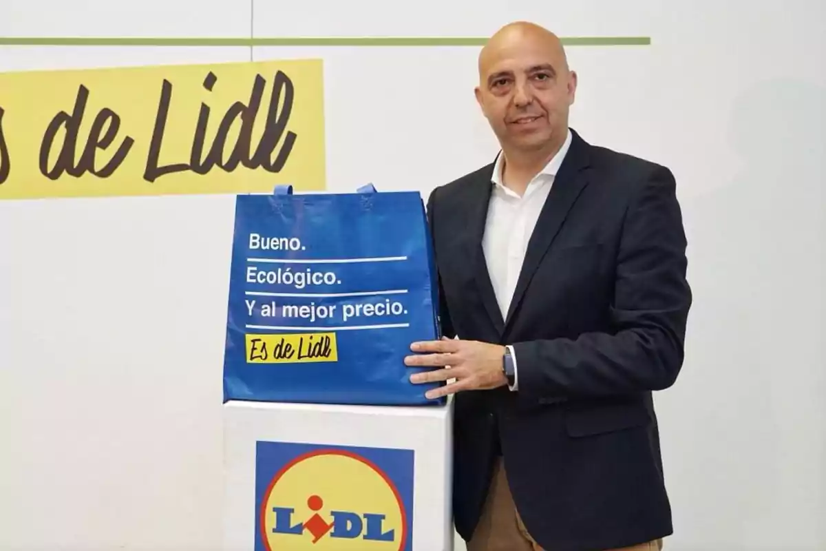 Un hombre de traje sostiene una bolsa azul con el logo de Lidl y un mensaje promocional. Un hombre de traje sostiene una bolsa azul con el logo de Lidl y un mensaje promocional.
