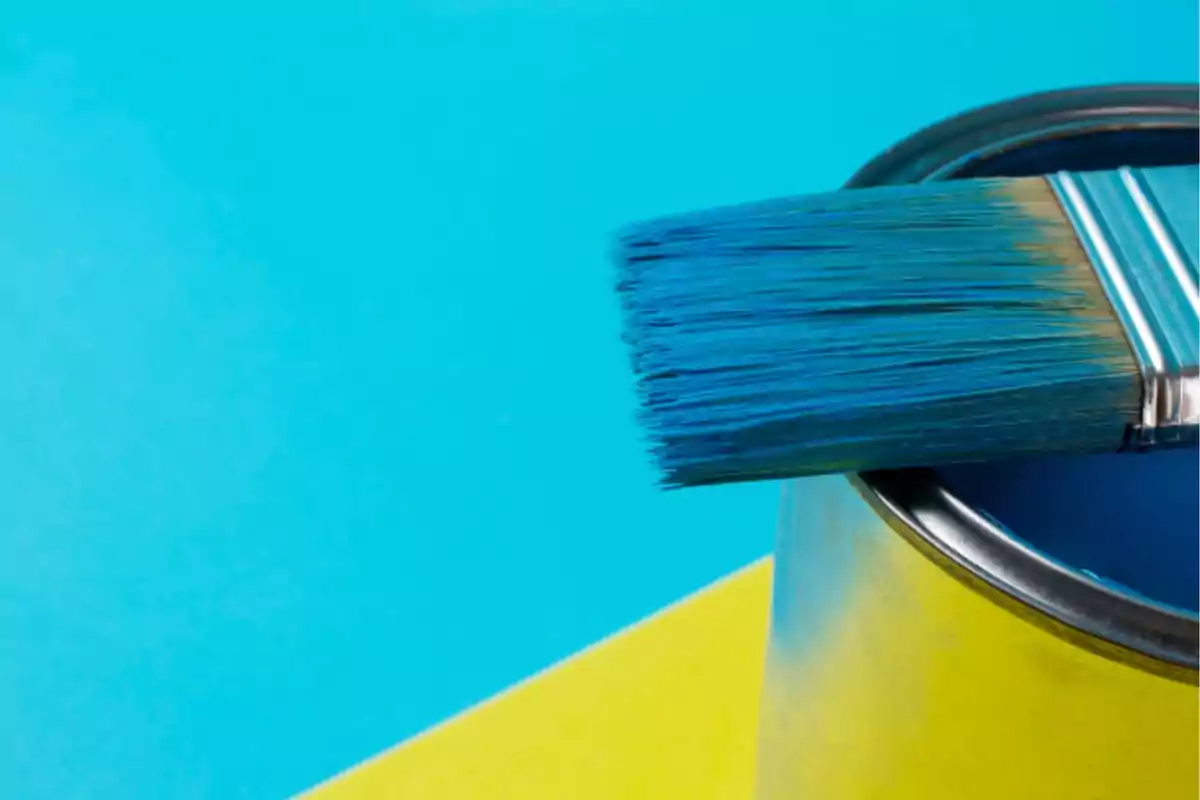 Brocha azul sobre lata de pintura con fondo azul y amarillo.