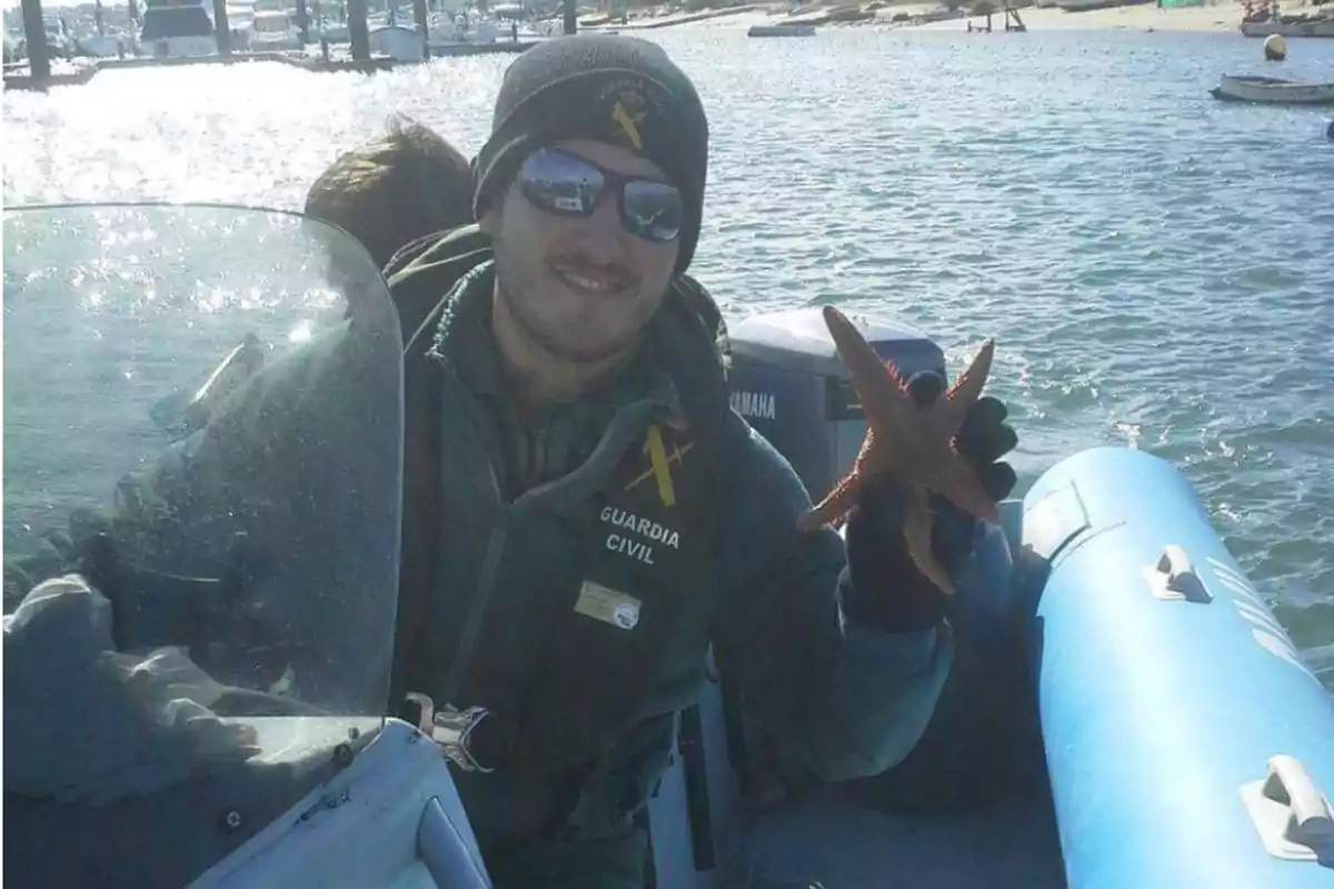 Un miembro de la Guardia Civil en una lancha sostiene una estrella de mar mientras navega en un entorno acuático. Un miembro de la Guardia Civil en una lancha sostiene una estrella de mar mientras navega en un entorno acuático.