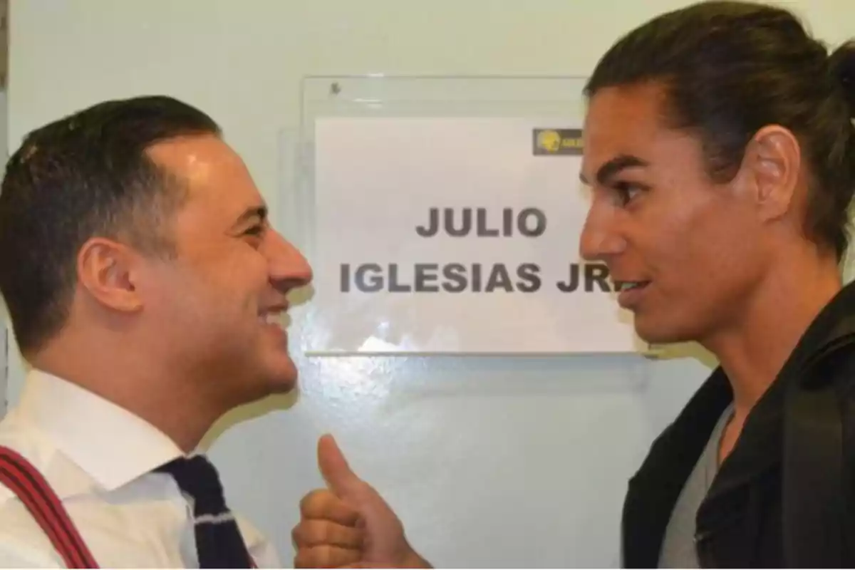 Dos personas conversando frente a un cartel que dice 