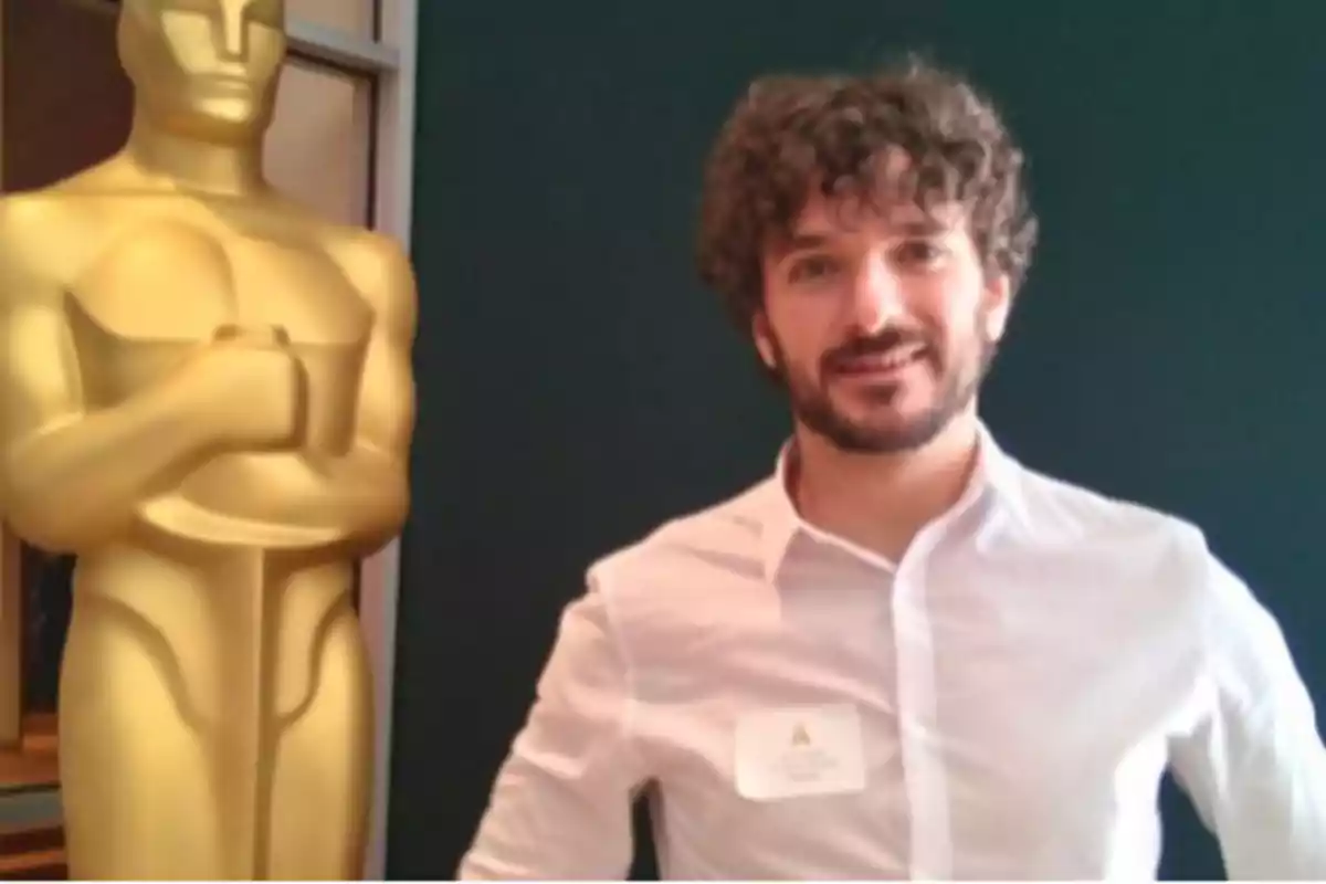 Un hombre de pie junto a una gran estatua dorada de un premio.