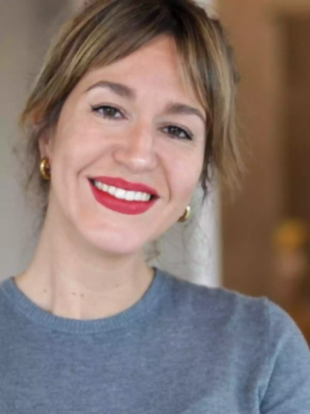 Una persona sonriendo con un suéter gris y labios rojos. Una persona sonriendo con un suéter gris y labios rojos.