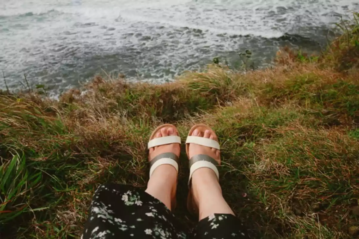 Persona sentada en un acantilado con sandalias mirando al mar.