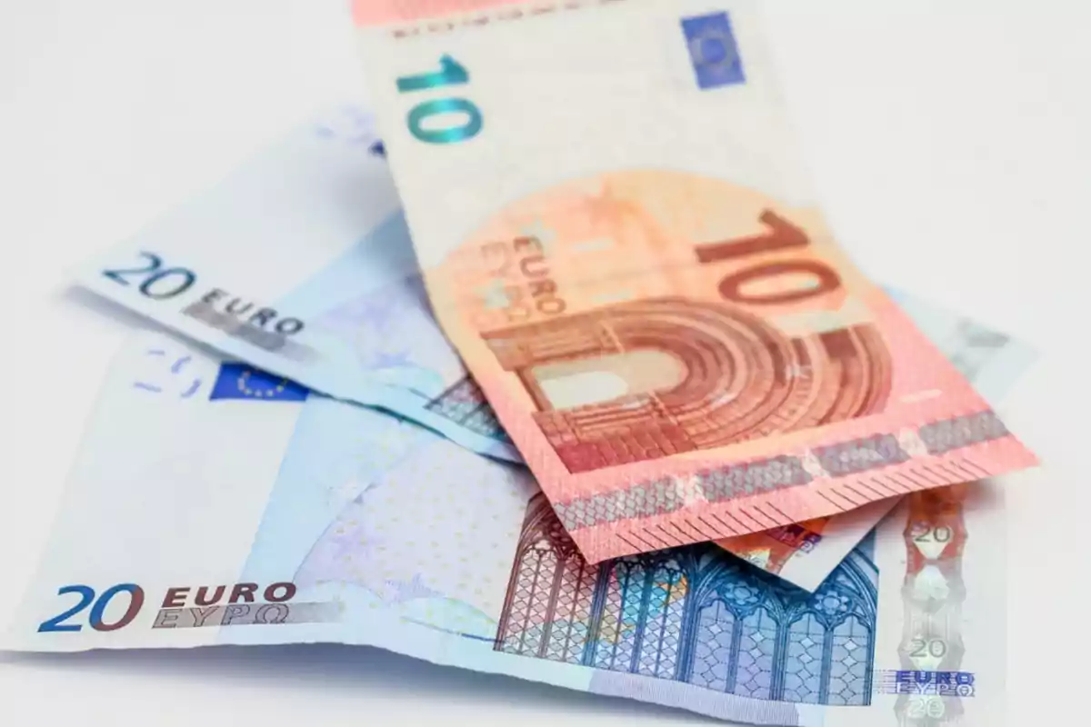 Billetes de euro de diferentes denominaciones apilados sobre una superficie blanca.