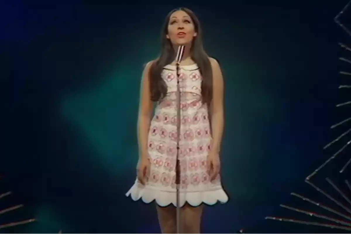 Mujer con vestido estampado cantando en un escenario con fondo oscuro.