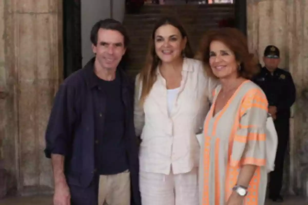 Tres personas posan juntas frente a un edificio con un guardia al fondo. Tres personas posan juntas frente a un edificio con un guardia al fondo.